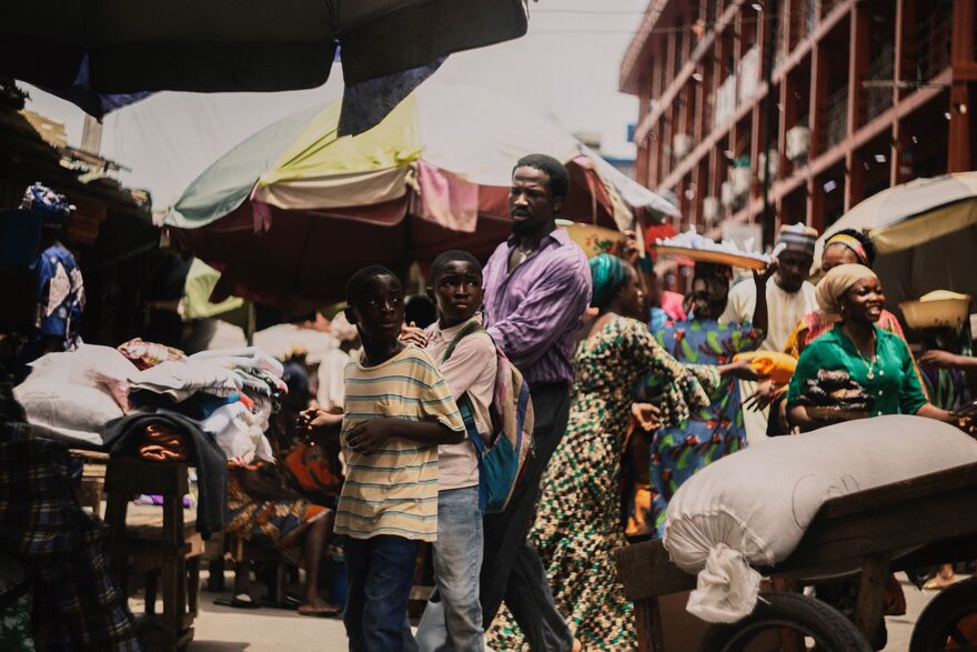A father leads two boys through a busy market in Lagos.
