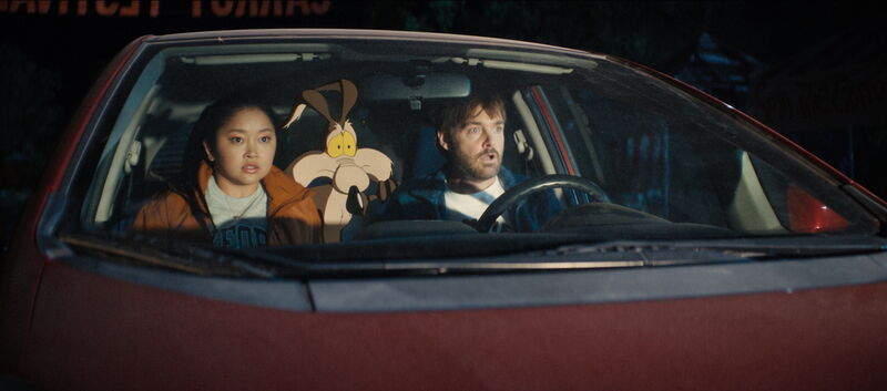 A woman, a cartoon coyote and a man in a car are startled as headlights shine on them