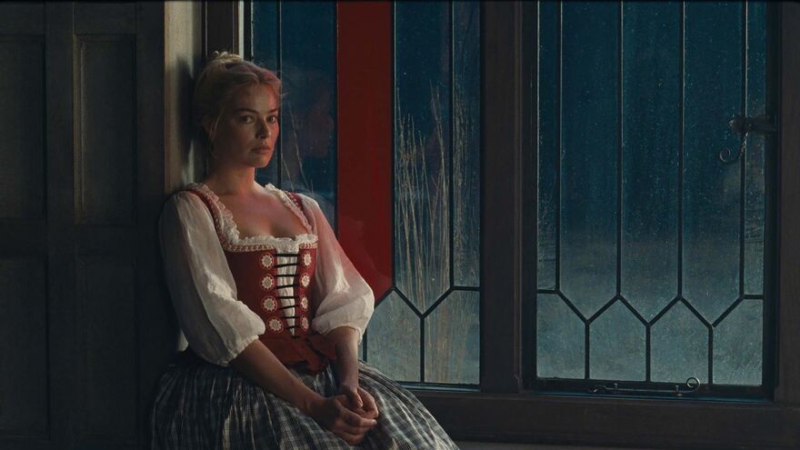 A pensive woman in a dress sits next to a large rainy window.