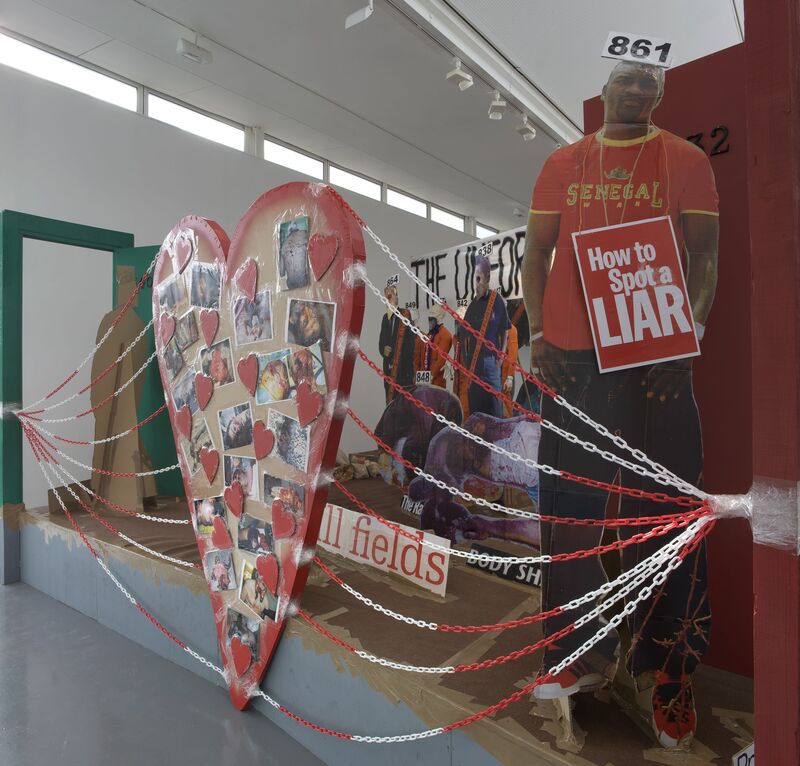 From Thomas Hirschhorn's exhibition. A cut-out of a man wearing a sign that says 'How to spot a Liar'. There is also a large cardboard love heart, with many image of people on it.