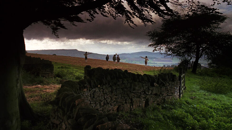 Two people have a pistol stand-off in a field in the countryside.