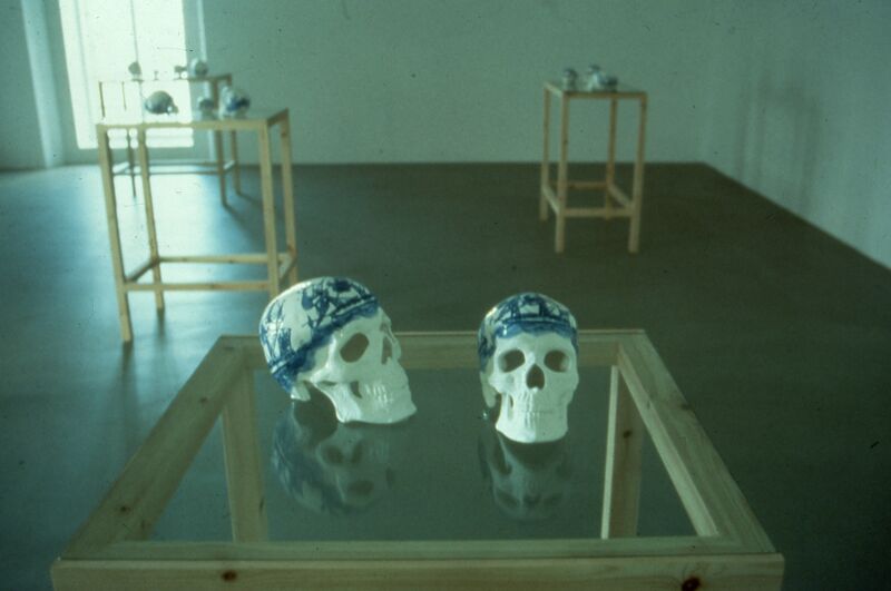 Two skulls sit on a glass table. The skulls are painted with blue designs.