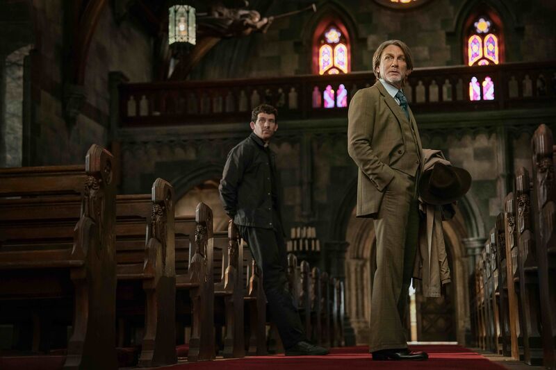 A detective and a priest stand in a church. 