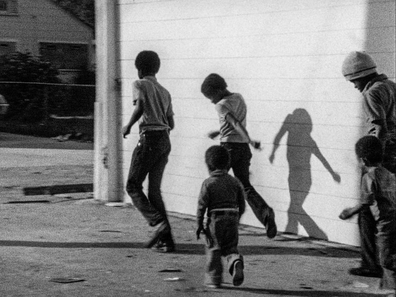 a black and white image of a group of young boys of different ages running along the street