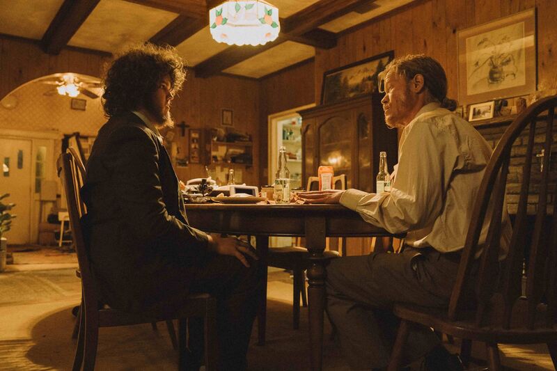 Two men sit a table in a family home with wooden walls and warm lighting