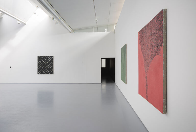 Image shows a brightly lit gallery two. We are looking along a wall to the right at a sharp angle, so we can see two paintings going off into the distance towards a corridor into gallery 1. The first painting is red and the second is green. Across the floorspace, to the left on the back wall we can see another artwork, which is also rectangular, but black. 