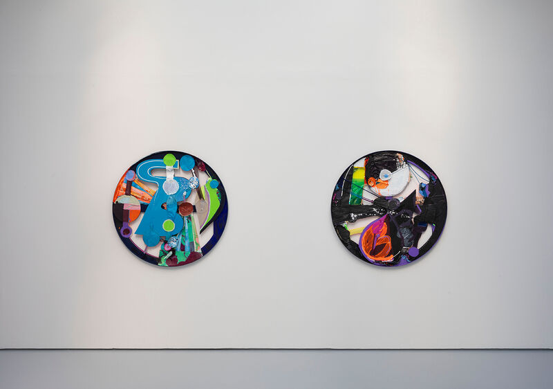 Two round artworks are shown on a white wall. Using found materials and canvas, they have a collaged appearance.