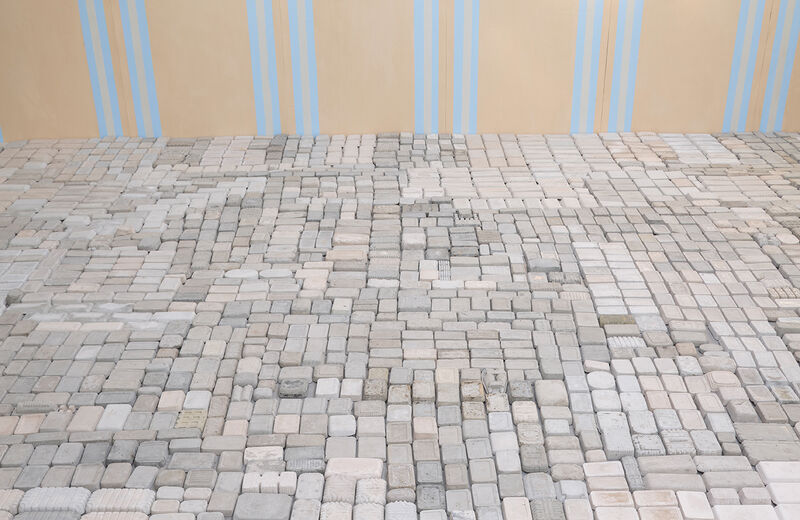 Photograph showing an installation including cast bricks laid out on the floor, and an orange and grey blue wall paper. 