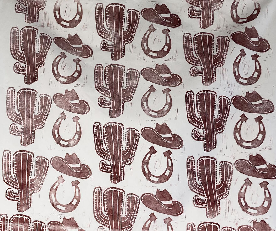 White fabric with repeat patten of cactus, cowboy hat and horse shoe in brown ink