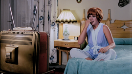 Woman looking worried while sitting on a bed and watching tv