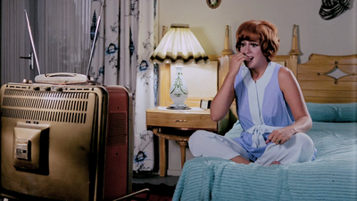 Woman looking worried while sitting on a bed and watching tv