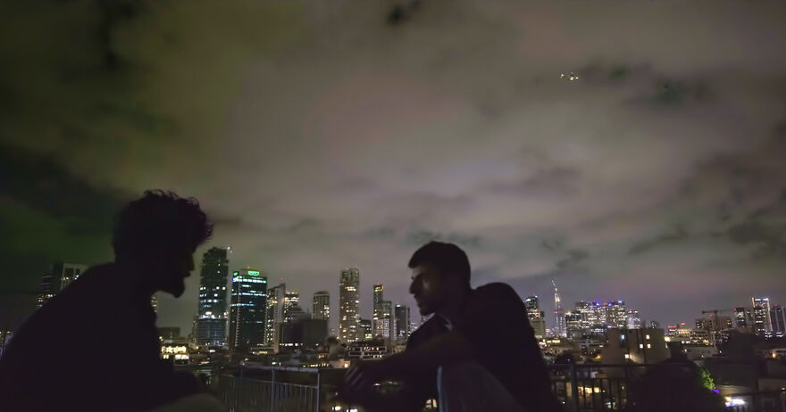 Two men stand on a city rooftop at night
