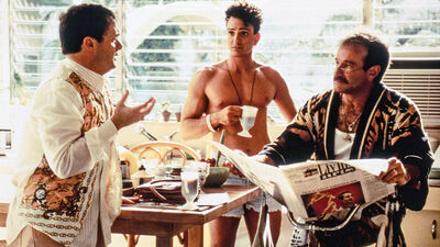 Three men, one shirtless, stand around a table at breakfast time.