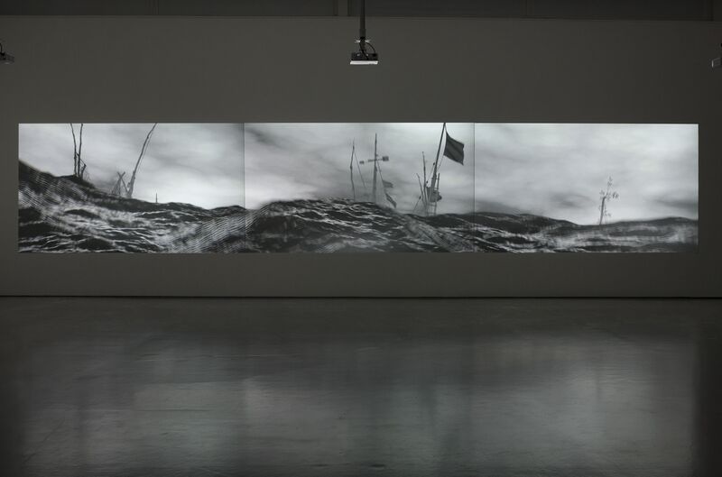 A projection in DCA Galleries as part of IC-98's exhibition shows a monochrome animation of a choppy seascape, with large mast with ruined flags emerging from the sea.