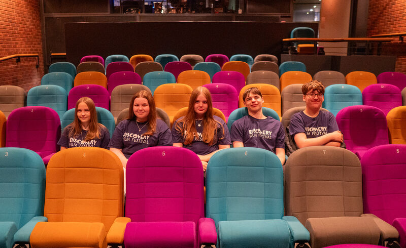 Five young people wearing Discovery Film Festival t-shirts sit in DCA Cinema.