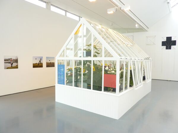 A white greenhouse sits in DCA Galleries. The greenhouse is filled with sunflowers and other flowers.