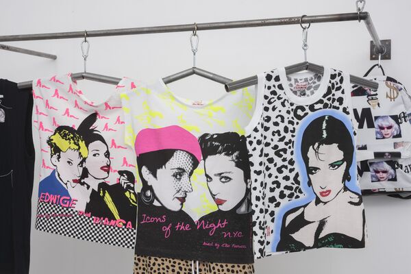 A close-up shot of 3 t-shirts which hang on a rack in DCA Galleries as part of 'Spring / Summer 2015' exhibition. They are neon and have pictures of Maripol on them. 