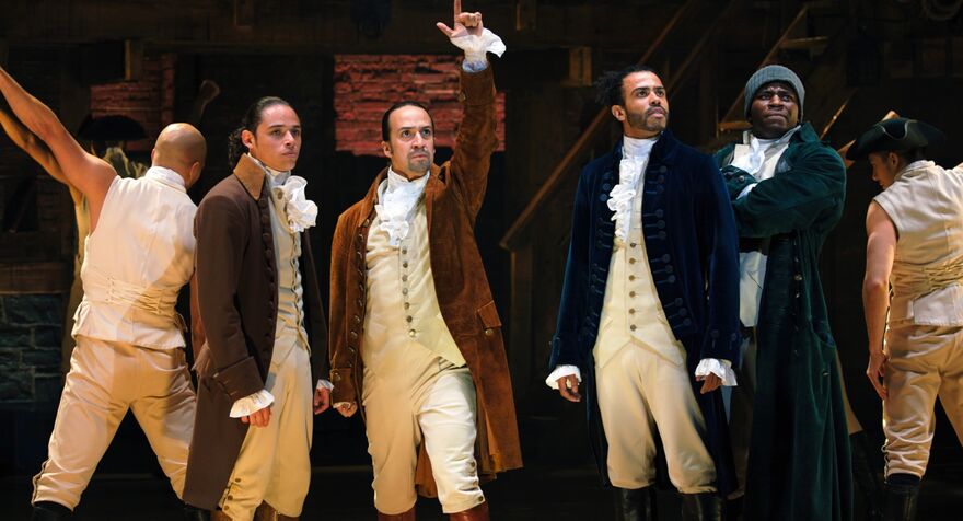 Men in 18th century clothing stand on stage in Hamilton.