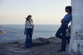 Two people stand outside on a bay, with a blue sea behind them