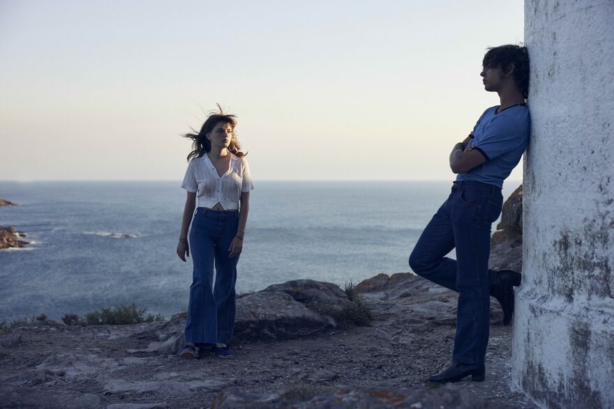 Two people stand outside on a bay, with a blue sea behind them