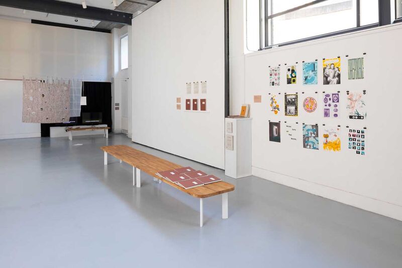 A gallery space with colourful prints on the wall and a bench in the foreground