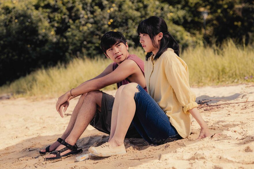 Two people sit on a beach together talking.