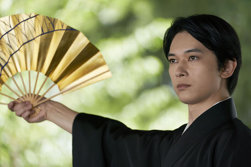 A Japanese man holds a golden fan. 