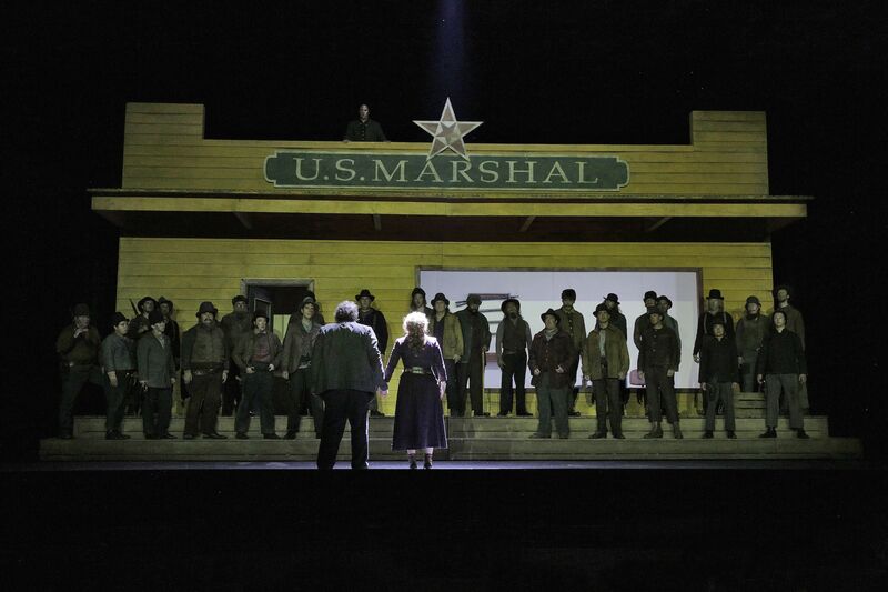 Opera stage filled with singers in western costume.