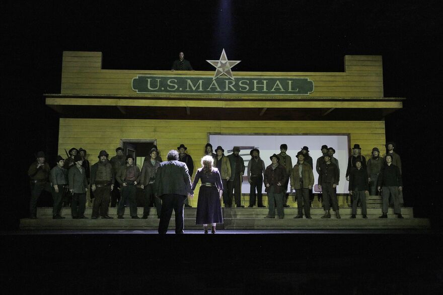 Opera stage filled with singers in western costume.