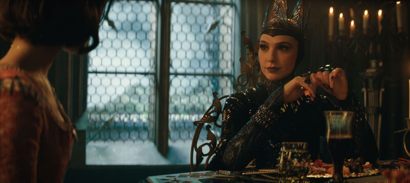 The evil queen from Snow White sits at a dining table.