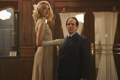 A short man with a comb over stands next to a tall blonde woman in an evening gown