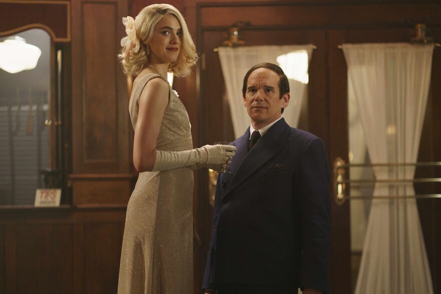 A short man with a comb over stands next to a tall blonde woman in an evening gown