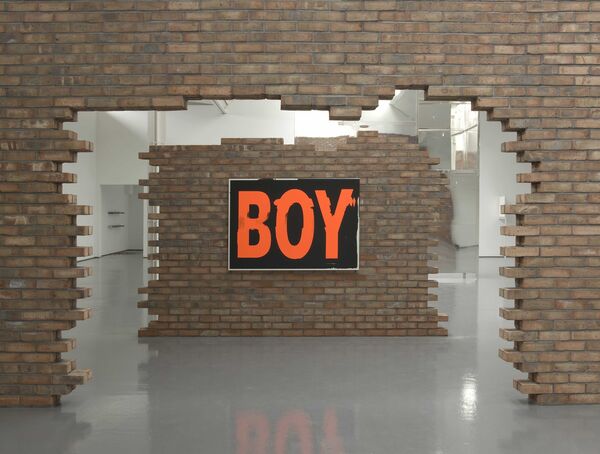 Two large, incomplete brick walls from Scott Myles' exhibition at DCA.. The second wall frames the other, and a black canvas hangs on it that says 'BOY' in bright orange writing.