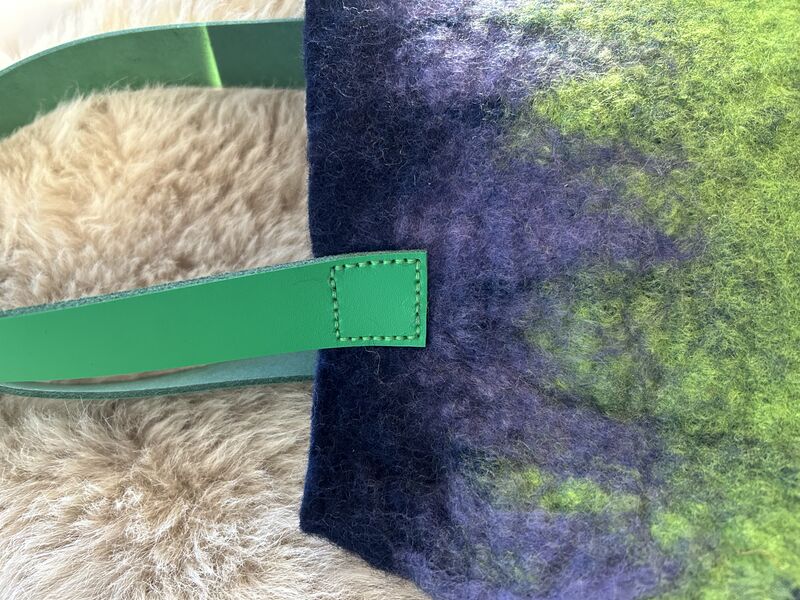 Close up of felted bag showing stitch detail where green leather strap attached to green and blue felted bag