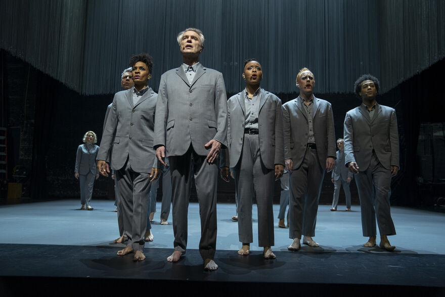 Musicians on stage singing in grey suits.