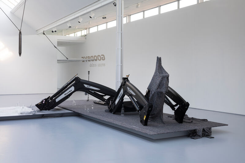 A gallery space, showing the image of farm equipment on a low plinth small glass sculptures also in view 