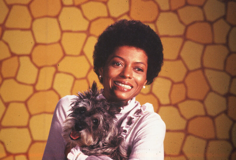 A young Diana Ross smiles at the camera while holding a small dog