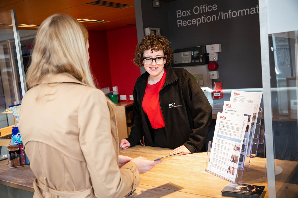 A Visitor Assistant looks at the cinema times with a customer.