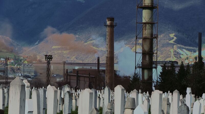 White gravestones stand in front of a large factory.