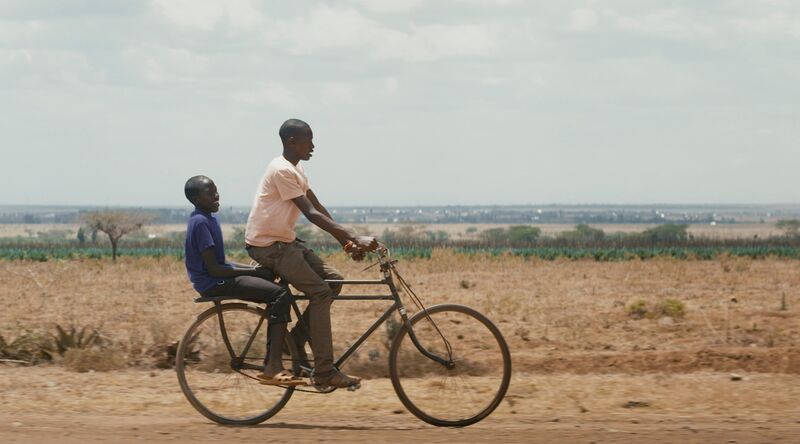 Two boys ride a bicycle together through a desert plain.