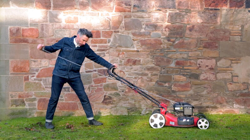 A man pushes a lawn mower with his arms outstretched
