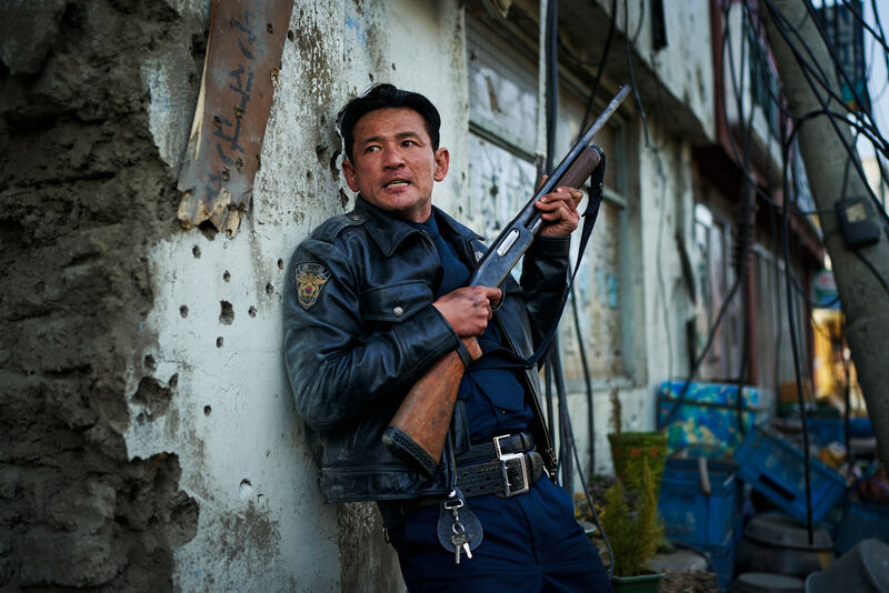 A police officer with a gun takes cover against a half-destroyed wall