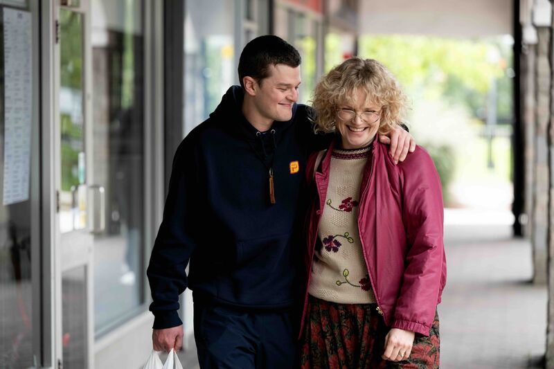 A young man and an older woman walk down the street together laughing