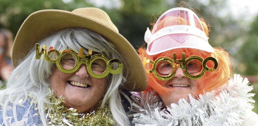 Two people dressed up in hats, wigs, novelty glasses and tinsel