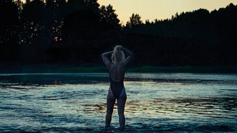 A woman in a swimming costume stands at dawn looking at a body of water