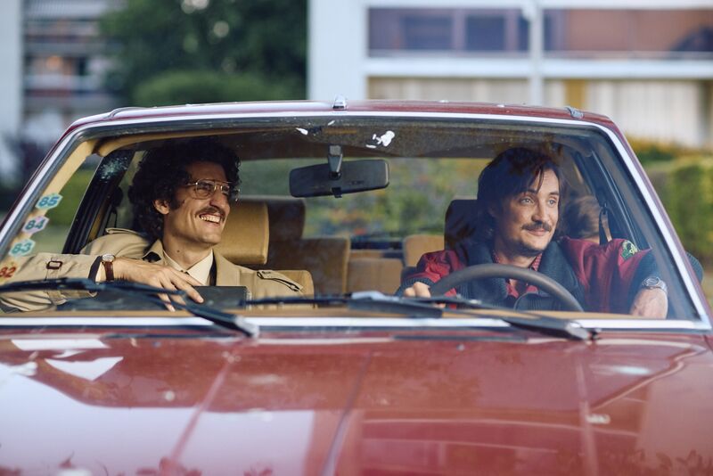 Two men with moustaches in a car
