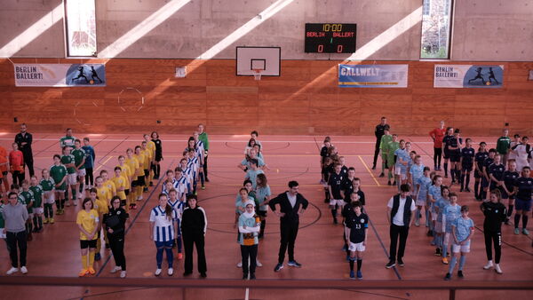 A school hall with lines of pupils in different sporting uniforms 