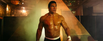 A muscular man with dark hair walks to a wrestling ring.