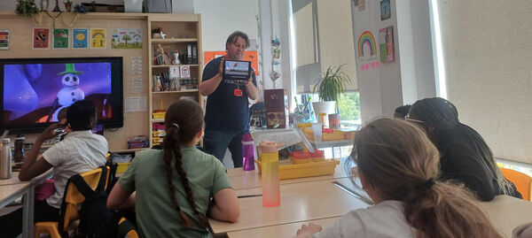 DCA staff member holding up an ipad infront of a classroom of primary pupils