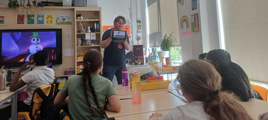 DCA staff member holding up an ipad infront of a classroom of primary pupils